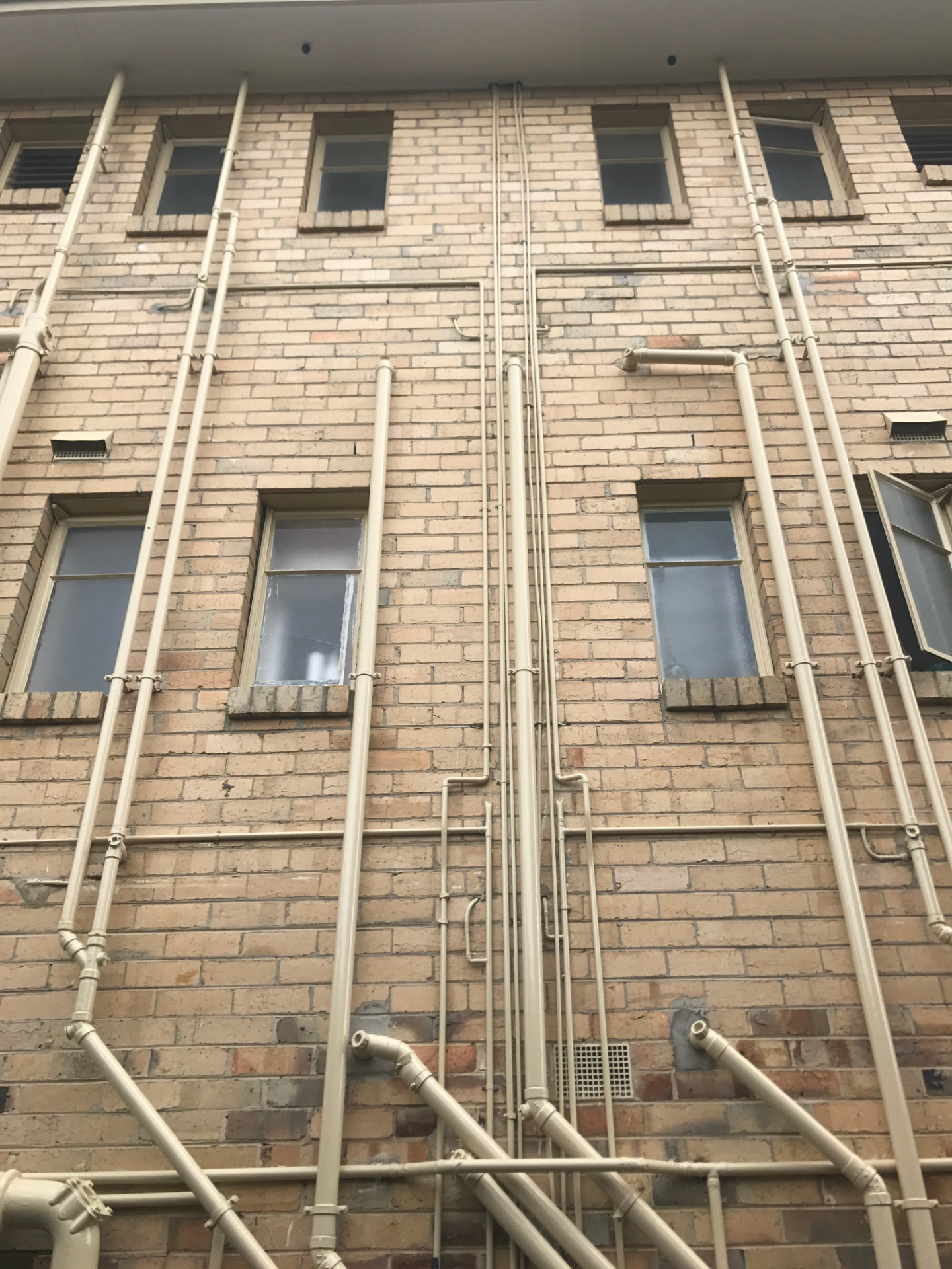 Exposed sewer and vent stacks running up a brick apartment building facade in Melbourne